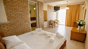 A hotel room with a brick wall, a bed with white linens, a desk with a vase of flowers, and a television mounted on the wall. - Blue Escape (Nafplio)
