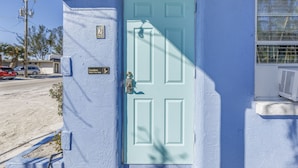Una puerta azul claro con un picaporte de latón, una pequeña señal encima y una ventana con una reja metálica a la derecha.