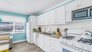 Una cocina moderna con armarios blancos, cocina a gas, microondas y una ventana con persianas.