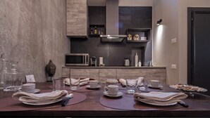 A modern dining area with a dark wooden table set for a meal, a kitchen in the background with a microwave and cabinets, and a Buddha statue on the left. - Cá delle Capriate, an intimate retreat at Cà d'Oro (Venezia)