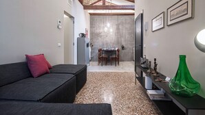 A modern living room with a dark sofa, a dining area with a table and chairs, and a kitchen area with a fridge and a green vase. - Cá delle Capriate, an intimate retreat at Cà d'Oro (Venezia)