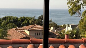 Une vue sur la côte, depuis une fenêtre ornée de tuiles en terre cuite, donnant sur un quartier résidentiel avec des maisons et offrant une vue dégagée sur la mer.