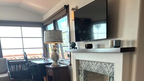 Une chambre d’hôtel moderne dotée d’un grand téléviseur à écran plat fixé au-dessus d’une cheminée, d’un bureau avec une lampe, d’un canapé confortable et offrant une vue sur l’extérieur grâce à de grandes fenêtres.