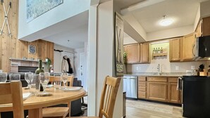 A modern kitchen with wooden cabinets, a black refrigerator, and a dining area with a wooden table and chairs. - BearNecessities- Pool, Hot Tub, Gym (Killington)