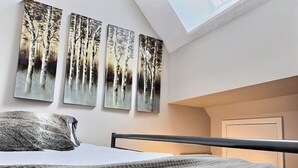A bedroom with a bed, a skylight, and three wall-mounted paintings of trees. - BearNecessities- Pool, Hot Tub, Gym (Killington)
