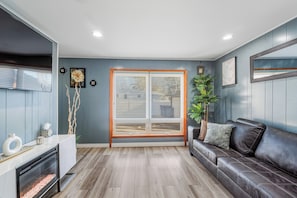 A modern living room with a large window, a fireplace, a leather sofa, and a minimalist decor style.