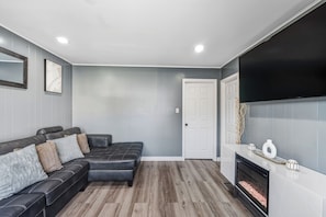 A modern living room with a sectional sofa, a fireplace, and a flat-screen TV mounted on the wall.