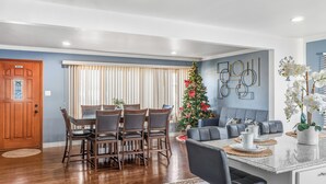 Un comedor con una mesa y sillas de madera, un árbol de Navidad y una zona de estar con sofá y mesa de centro.