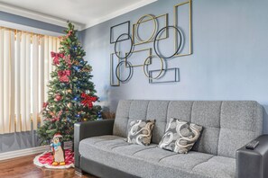 A living room with a grey sofa, patterned cushions, a Christmas tree, and a wall with geometric decor.