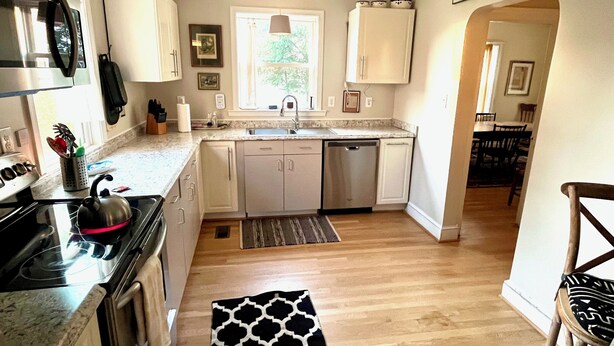 A compact kitchen with white cabinets, a stainless steel dishwasher, and a black kettle on the stove. - Fabulous Farm Stay (Crozier)