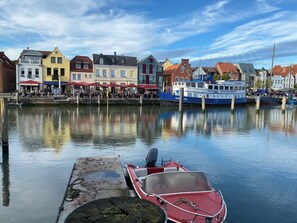 Ein Ufer mit einer Reihe bunter Gebäude, eine Anlegestelle mit einem kleinen Boot und ein größeres Boot im Hintergrund.