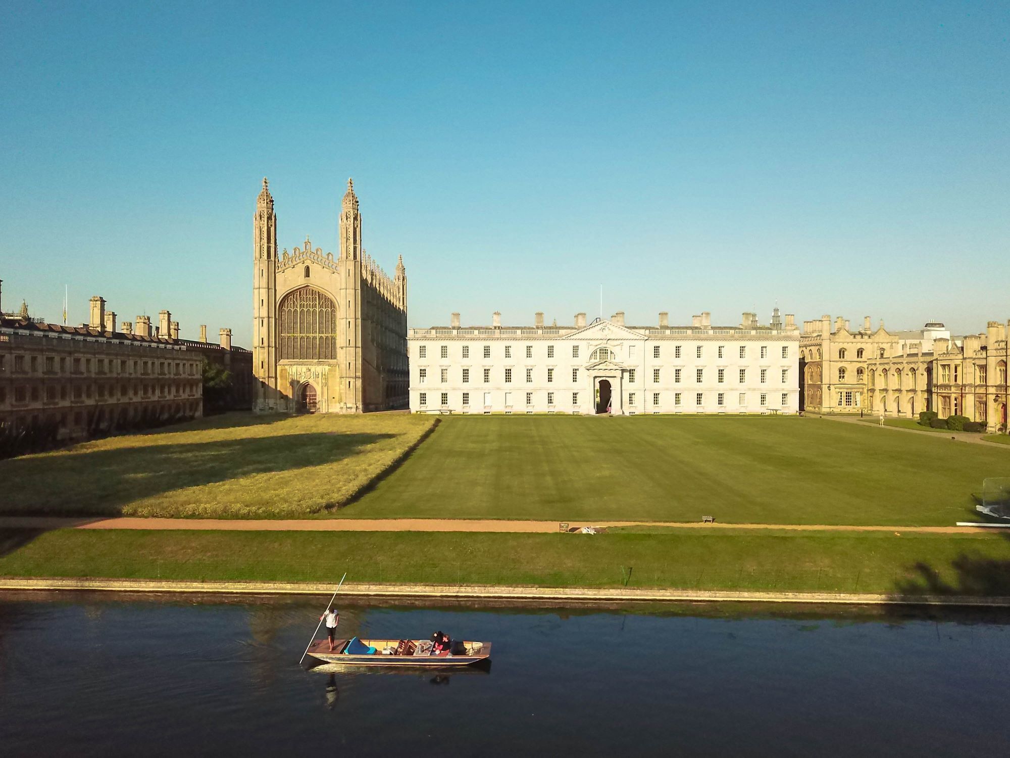 A large historic building with a central entrance, surrounded by a well-maintained lawn and a body of water with a rowboat.