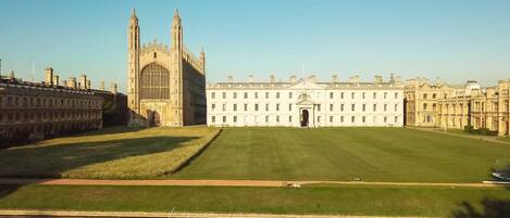 A large historic building with a central entrance, surrounded by a well-maintained lawn and a body of water with a rowboat.