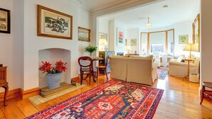 A spacious living room with a large rug, a fireplace, and a dining area with chairs and a table. - Pass the Keys | Charming Cottage in the City Centre | Free Parking (Cambridge)