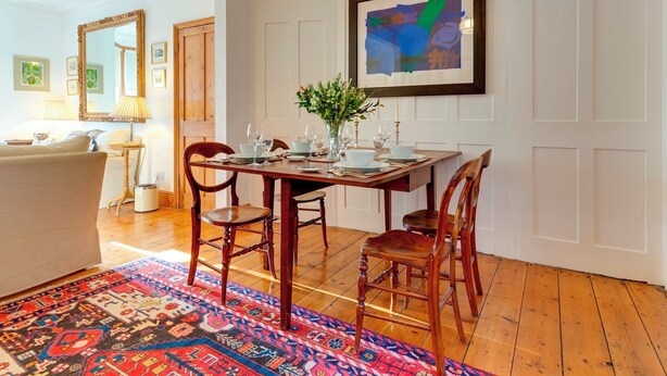 A dining area with a wooden table set for four, surrounded by chairs, a patterned rug, and a framed abstract painting on the wall. - Pass the Keys | Charming Cottage in the City Centre | Free Parking (Cambridge)