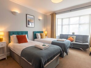 Two single beds with matching headboards and white bedding, flanked by nightstands and a sofa, in a clean and inviting space.