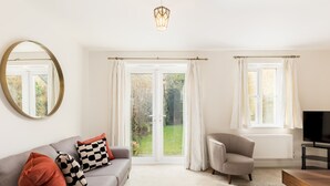 Ein Wohnzimmer mit grauem Sofa, einem runden Spiegel, einem grauen Sessel, einem Holztisch und einem Fernseher.