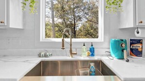 A modern kitchen with a large window, stainless steel sink, and various toiletries on the counter.