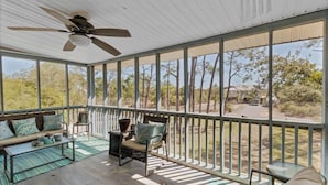 A covered outdoor area with a ceiling fan, a sofa with cushions, a chair, and a small table.