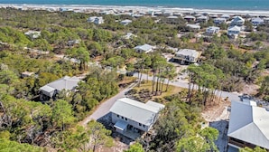 A coastal residential area with houses surrounded by dense trees and a beach in the background.