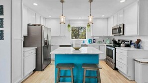 A modern kitchen with white cabinets, stainless steel appliances, a central island with bar stools, and pendant lighting.
