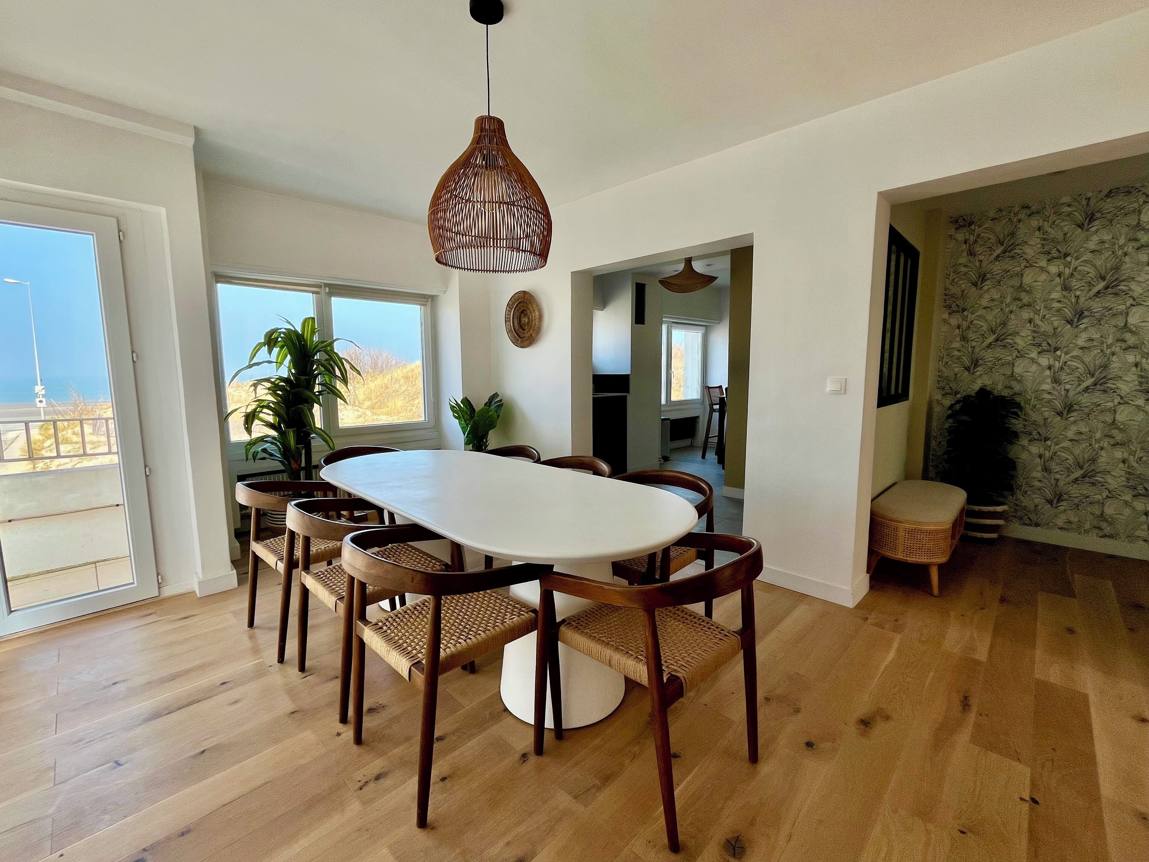 A dining area with a round table, six chairs, a hanging light fixture, and a view through a glass door to the outdoors.