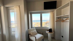 Quarto com vista para a praia, uma cadeira, uma mesinha com uma cafeteira e uma TV fixada na parede.