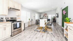 Uma cozinha moderna com eletrodomésticos de aço inoxidável, uma área de jantar com mesa e cadeiras de vidro, e uma sala de estar com lareira.