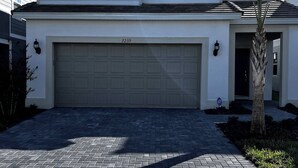 A two-story house with a garage, a brick driveway, and a small tree in the front yard. - Your Home by the Orlando Parks (Davenport)