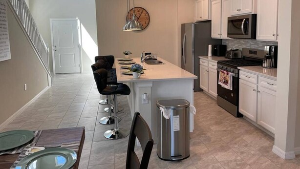 A modern kitchen with white cabinets, stainless steel appliances, and a central island. - Your Home by the Orlando Parks (Davenport)
