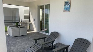 An outdoor patio with a grill, wicker furniture, and Adirondack chairs. - Your Home by the Orlando Parks (Davenport)