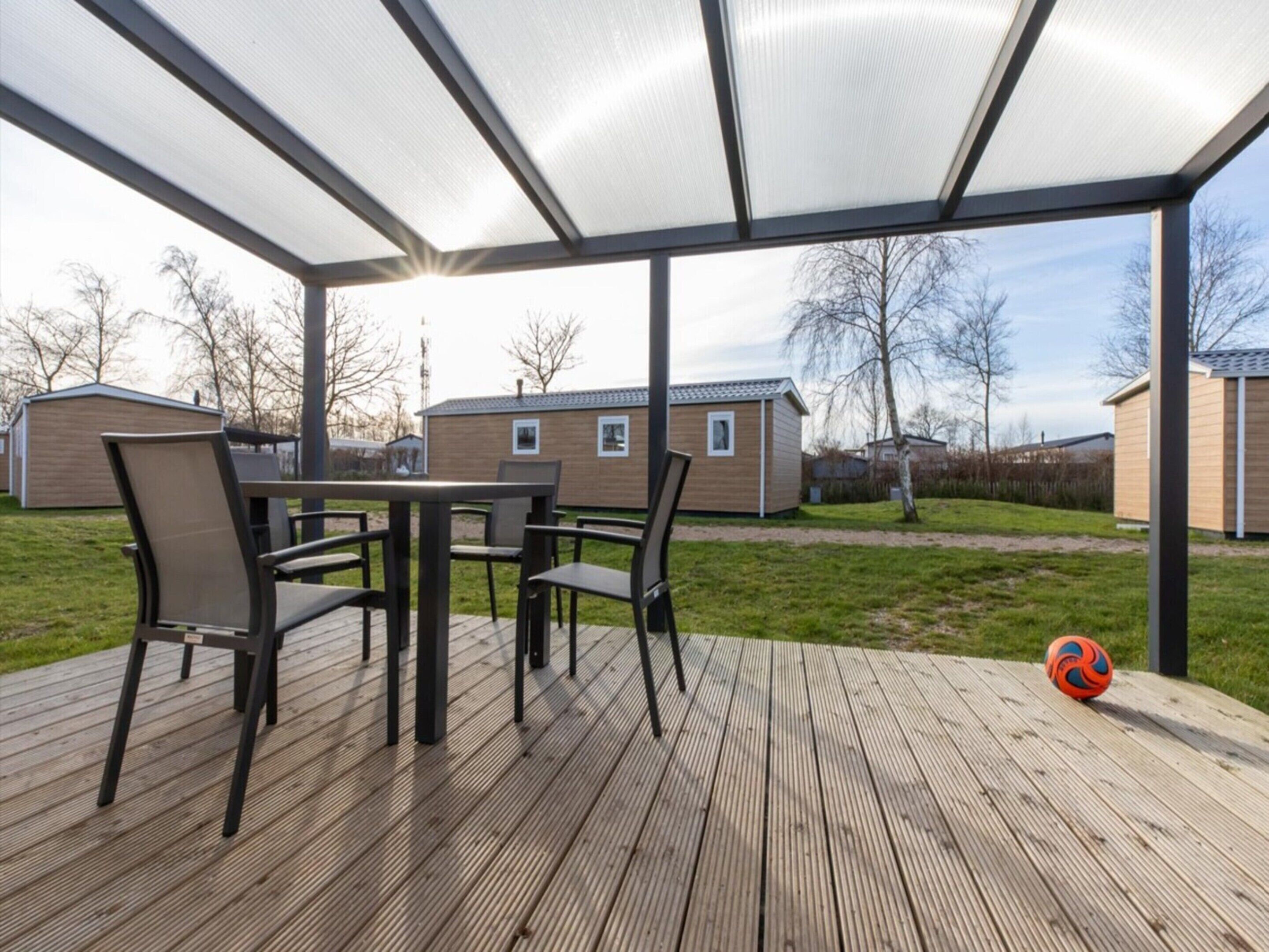 An outdoor patio with a table and chairs, a volleyball, and a covered area with a view of houses in the background.
