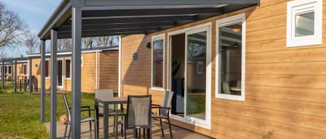 A modern mobile home with a covered patio area, large windows, and a deck.