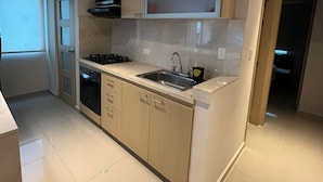 Una cocina moderna con armarios de madera clara, un lavamanos de acero inoxidable y un microondas integrado.