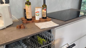 Une cuisine équipée d’un lave-vaisselle, d’une machine à café et d’une planche à découper en bois sur laquelle se trouvent des bouteilles et une boîte de conserve.