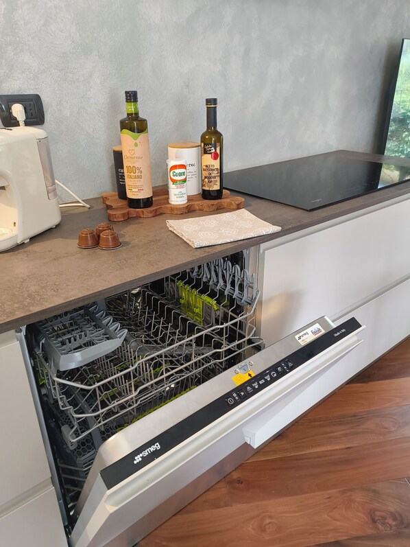 A kitchen with a dishwasher, a coffee maker, and a wooden cutting board with bottles and a can on it. - Relaxing Break Lario (Gravedona)