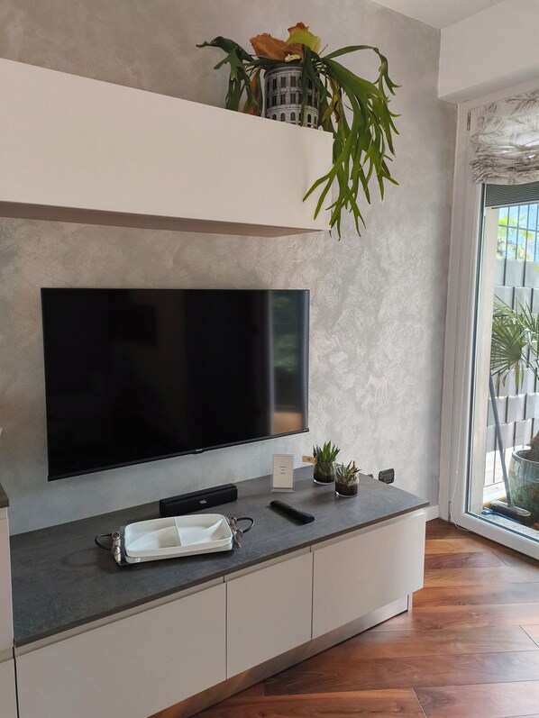 A modern living room with a flat-screen TV mounted on a wall, a white console table with a remote control, a small potted plant, and a decorative vase. - Relaxing Break Lario (Gravedona)