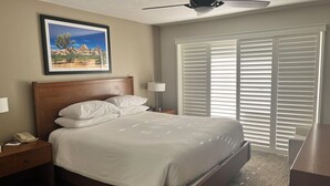 Ein ordentlich bezogenes Bett mit weißen Leinen, ein Holz-Kopfteil, ein Nachttisch mit Telefon, Lampe und Deckenventilator.