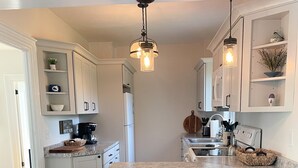 Una cocina con armarios blancos, una isla central con taburetes, una cafetera e iluminación colgante.