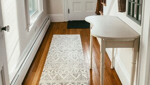 Un pasillo con una puerta blanca, suelo de madera y una mesa blanca junto a una ventana verde.