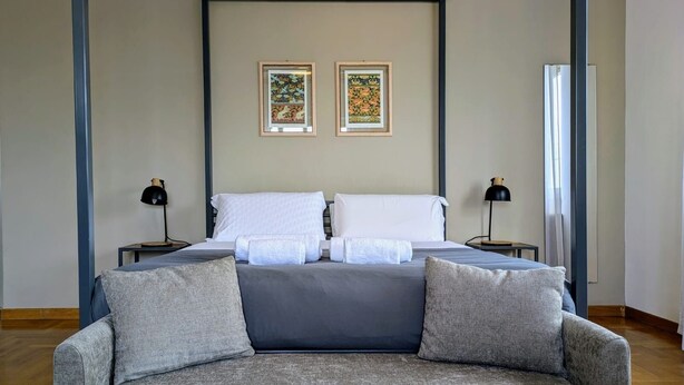 Une chambre à coucher comprenant un lit, deux tables de chevet, un canapé gris et deux œuvres d’art encadrées accrochées au mur.