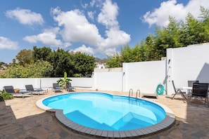 A swimming pool with lounge chairs and a hose reel, surrounded by a white wall and greenery. - Casa Torremuelle II | Pool & BBQ Townhouse (Benalmádena)