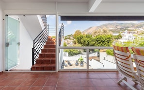 A balcony with a view of a hillside town, a glass door leading to a tiled floor, and a set of stairs with a metal railing. - Casa Torremuelle II | Townhouse with Private Pool & BBQ (Benalmádena)