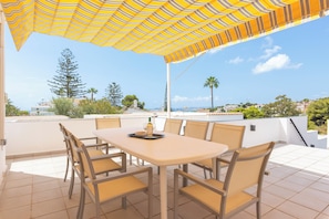 A rooftop terrace with a table and chairs, a striped umbrella, and a view of the city and hills. - Casa Torremuelle II | Pool & BBQ Townhouse (Benalmádena)