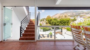 A balcony with a view of a hillside town, a set of stairs leading to an upper floor, and a glass door. - Casa Torremuelle II – Townhouse with private Pool & BBQ near Playa Bonita (Benalmádena)