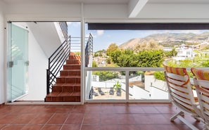 A balcony with a view of a hillside town, a set of stairs leading to an upper floor, and a glass door. - Casa Torremuelle II – Townhouse with private Pool & BBQ near Playa Bonita (Benalmádena)