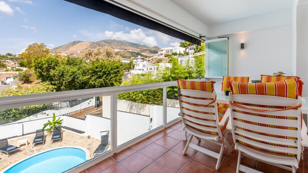 A balcony with a view of a mountainous landscape, a swimming pool, and white striped chairs. - Casa Torremuelle II – Townhouse with private Pool & BBQ near Playa Bonita (Benalmádena)