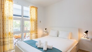 A hotel room with a bed, curtains, a bedside lamp, and a view of the outdoors. - Casa Torremuelle II – Townhouse with private Pool & BBQ near Playa Bonita (Benalmádena)