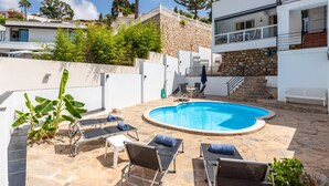 A swimming pool with lounge chairs, a stone patio, and a white building with a stone wall and balcony. - Casa Torremuelle II – Townhouse with private Pool & BBQ near Playa Bonita (Benalmádena)