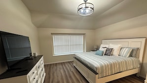 Ein Schlafzimmer mit Bett, Fernseher, Fenster mit Jalousien, Deckenventilator und Kommode.